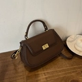 Détail du sac en cuir grainé avec fermoir rotatif doré posé sur un bureau en bois brun - Marron
