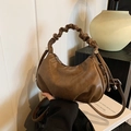 Bolso de media luna marrón plisado con asa de nube y correa ajustable sobre un libro - Arena