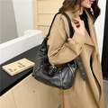 Retro black leather hobo bag with gold hardware and rivets worn over a trench coat - Black