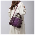 Detail of a dark purple crocodile pattern tote bag shown with a white trench coat - Purple