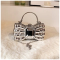 Macro detail of silver bow evening bag with black gem inlay on white plush texture - Silver