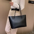 Minimalist black tote bag with chain handles shown as a crossbody on a stylish model - Black