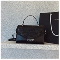 Minimalist black leather handbag with textured flap and silver metal lock on stone step - Black