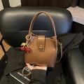 Sac seau vintage en cuir marron avec fermoir doré et pendentif cerise sur chaise - Style avec pendentif cerise / Marron