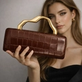 Detail of dark brown crocodile pattern clutch with elegant gold wavy metal handle - Coffee