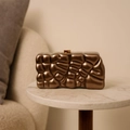 Detail of creative pleated bronze acrylic clutch with metallic texture on white marble - Coffee