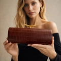 Brown crocodile embossed baguette bag with golden crescent buckle held by model - Coffee