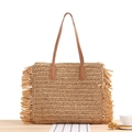 Beige Strohtasche mit Fransen und braunen Ledergriffen auf einer Holzoberfläche serviert - Camel