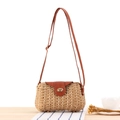 Straw woven crossbody bag with brown leather flap and golden twist lock on wood table - Camel