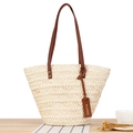 Beige geflochtene Stroh-Tote-Bag mit braunen Ledergriffen auf rustikalem Holztisch - Beige