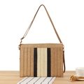 Striped woven paper straw crossbody bag in tan black and cream on a wooden desk - Camel