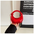 Mini red metallic crescent bag with circular handle and gold chain strap held by hand - Red