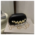 Detail of black oval acrylic evening bag featuring a gold wavy metal handle and snake chain - Black