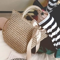 Detail einer Strohhandtasche mit großer champagnerfarbener Seidenschleife und Naturtextur - Khaki