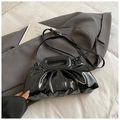 Detalle de bolso plisado negro brillante con asa metálica sobre tela gris - Negro