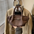 Braune Umhängetasche in Eimerform mit Metalldetail vor minimalistischem Hintergrund - Lila