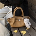 Tan leather bucket bag with side wings and plush bunny charm on autumn wood bench - Light Brown With Pendant