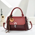Détail du sac bandoulière rouge avec texture tissée et breloque en forme de bretzel - Bordeaux