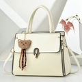 Elegant off-white structured handbag with gold hardware and brown bear charm - White
