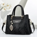 Detalle de bolso negro con patrón de serpiente, colgante de hoja dorada y perlas - Negro