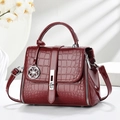 Close-up of glossy burgundy crocodile pattern handbag with silver clover pendant charm - Wine Red