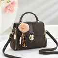 Deep brown matte crossbody handbag with gold hardware and plush charm on a stone stand - Coffee