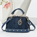 Dunkelblaue Handtasche mit Schlangenprägung, Goldnieten und Herzanhänger vor Dekor - Blau