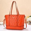 Detail view of bright orange quilted tote bag with golden logo plate and fine stitching - Red
