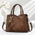 Detailed view of brown handbag with rhombus pattern, flower charm and knotted handle - Coffee