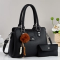 Détail du sac noir grainé avec boucle logo M et pompon décoratif sur fond neutre - Noir