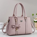 Detalle de bolso tote en cuero rosa claro con colgante de lazo y herrajes dorados - Rosa