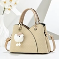 Beige Tote-Tasche mit V-Webstruktur, goldener Hardware und Plüschanhänger im weißen Setting - Khaki