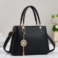 Detail of black pebbled leather tote with elegant gold metal pendant and sturdy handles - Black