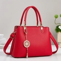Detail of red lychee leather handbag featuring golden hardware and decorative round pendant - Red
