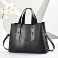 Detailed close-up of glossy black crocodile embossed handbag with gold metal hardware - Black