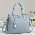 Close-up of light blue handbag with V-shaped metal logo and textured woven finish - Blue