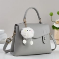 Gray pebble leather handbag with gold hardware and plush monster charm on studio background - Gray