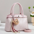 Detail view of pink textured handbag with plush bear charm and silver twist lock - Pink