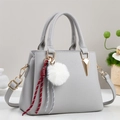 Close-up of light gray pebbled leather handbag with plush ball and woven strap detail - Gray