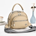 Minimalist beige shell crossbody bag with triple zippers and woven strap in daily setting - Light Khaki
