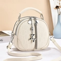 Detail of cream white textured crossbody bag featuring double zippers and a dog charm - White