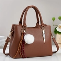 Brown litchi grain leather handbag detail with golden hardware and plush ball charm - Khaki/Earth Yellow