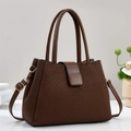 Close-up of brown textured leather handbag with gold metal buckles and woven pattern - Coffee