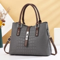 Grey crocodile embossed handbag with brown straps and silver clasp on a warm studio background - Gray