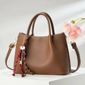 Detail of a dark brown pebble leather handbag featuring gold hardware and a tassel keychain - Brown
