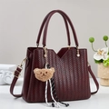 Large burgundy handbag with V-shaped weave texture and brown bear charm on a display - Red