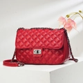 Close-up of red quilted leather shoulder bag with silver chain and twist lock on white stand - Red
