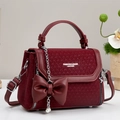 Detailed close-up of burgundy leather crossbody bag with bow pendant and star chain - Red