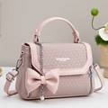 Detalle del bolso rosa con textura tejida, lazo 3D y colgante de cadena de perlas - Rosa