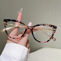 Dettaglio di occhiali cat-eye con motivi marmorizzati multicolore e stanghette in metallo oro - Montatura a fiori con lenti trasparenti e parti dorate